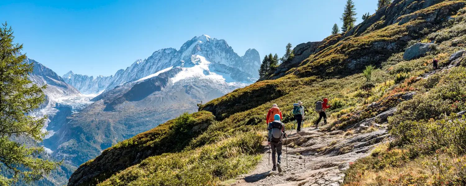 Randonneurs sur un sentier de montagne face aux sommets enneigés